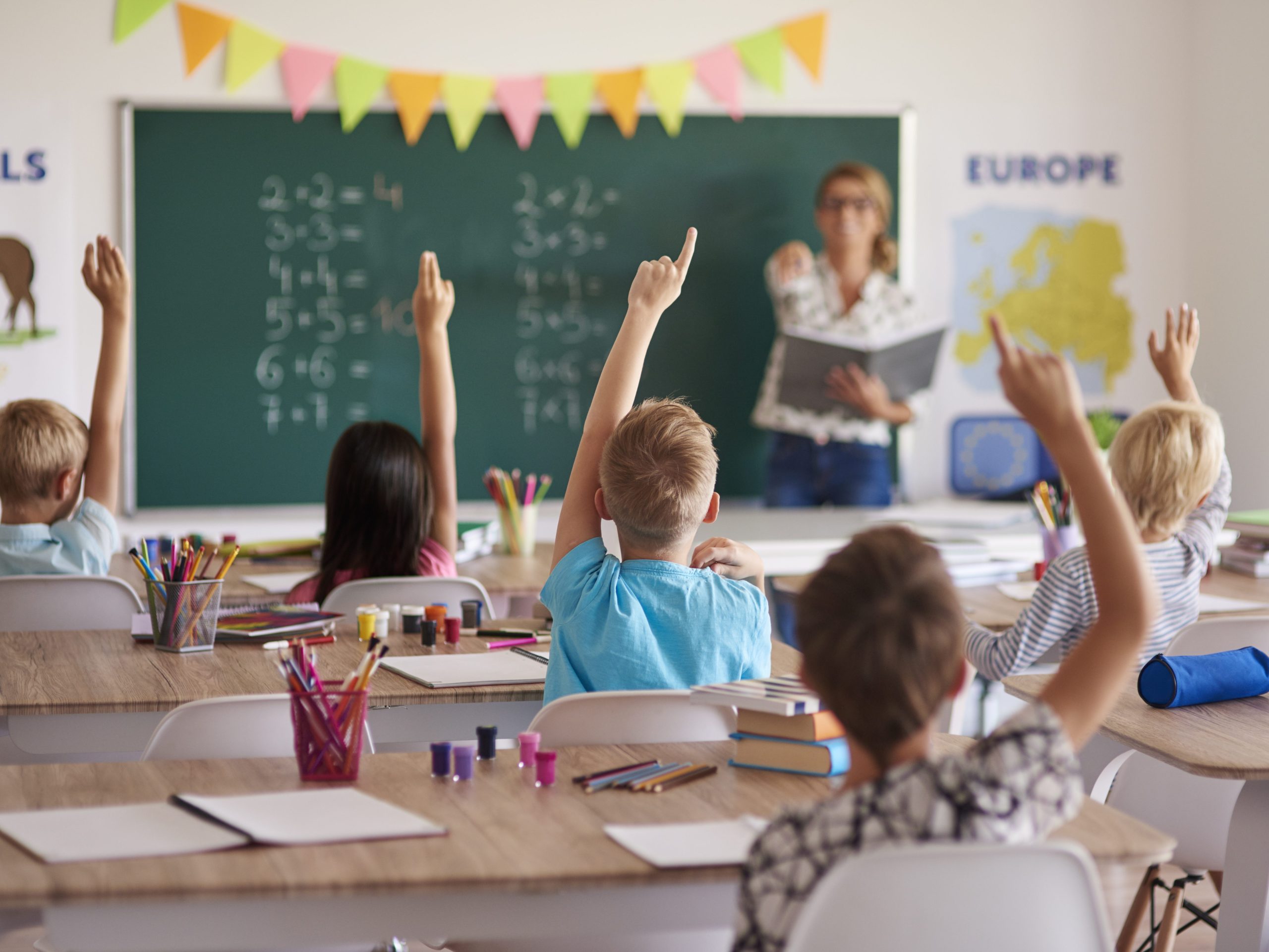 Alunos em sala de aula com a mão levantada para responder, simbolizando o engajamento promovido por estratégias de personalização na educação.